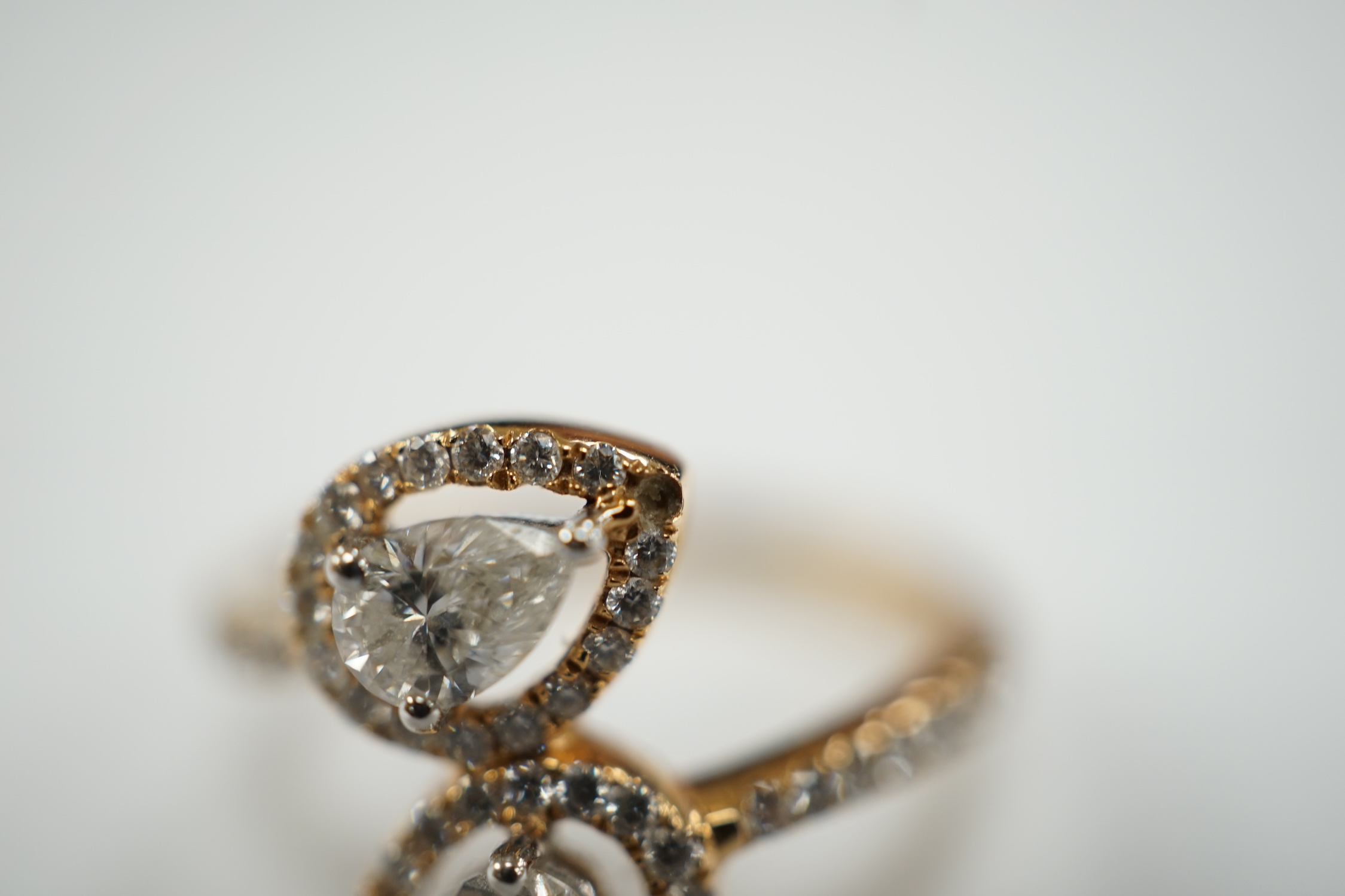 A modern 18k and two stone pear cut diamond set cross-over ring, with diamond chip border and shoulders, size L, gross weight, 2.9 grams.